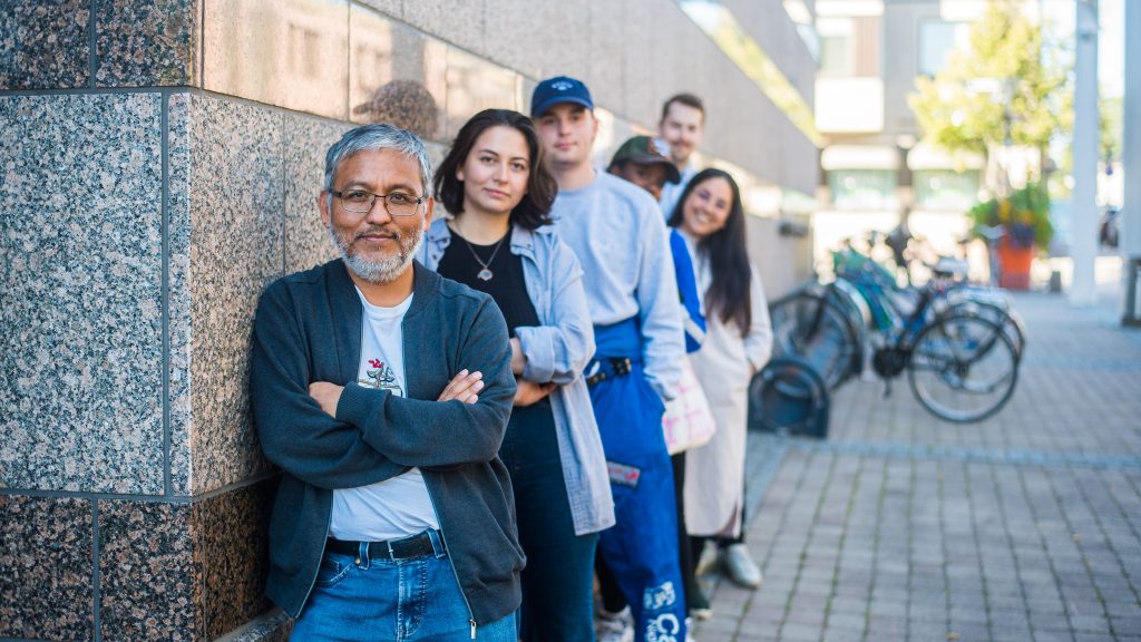 Six International Talents leaning on the wall and looking at the camera. On of them is wearing student overalls.