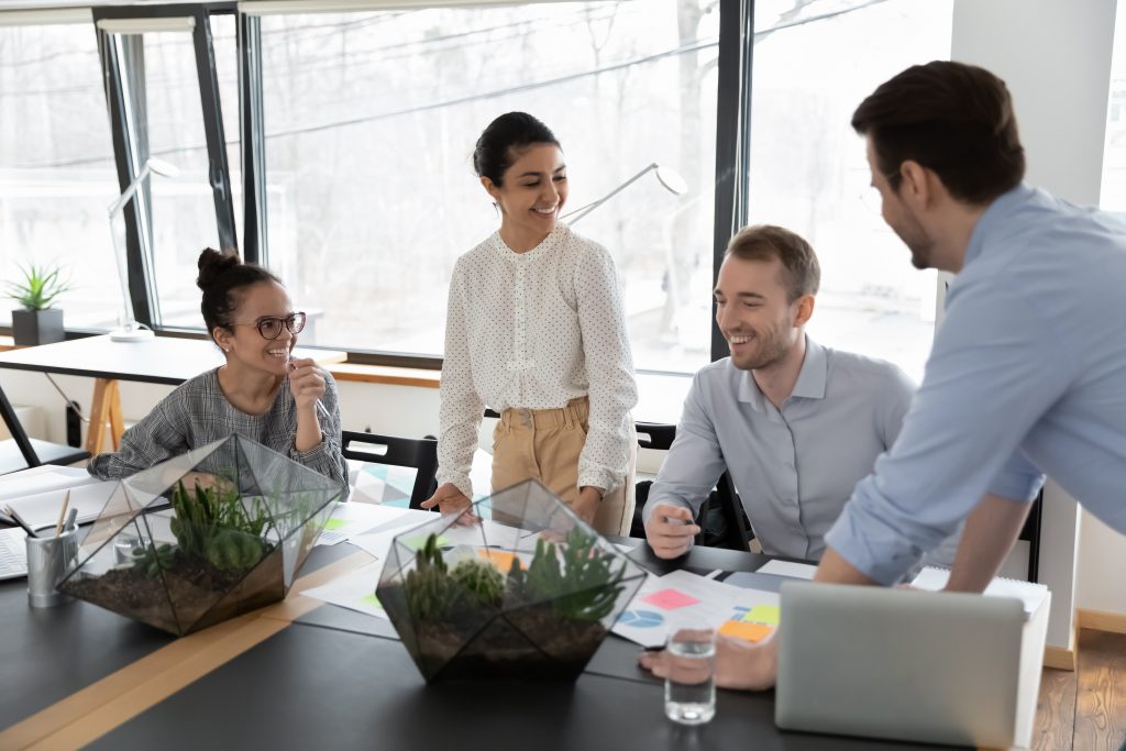 Smiling diverse multiethnic businesspeople sit at desk in office brainstorm discuss paperwork together, happy motivated multiracial colleagues cooperate consider financial document at meeting