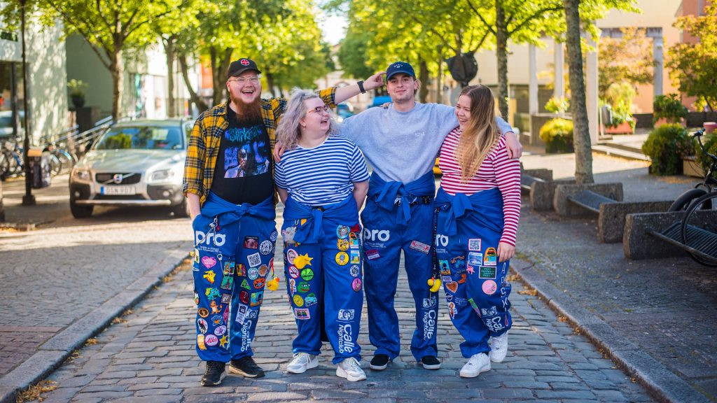Four students holding each other on a cobble stone street wearing student overalls.